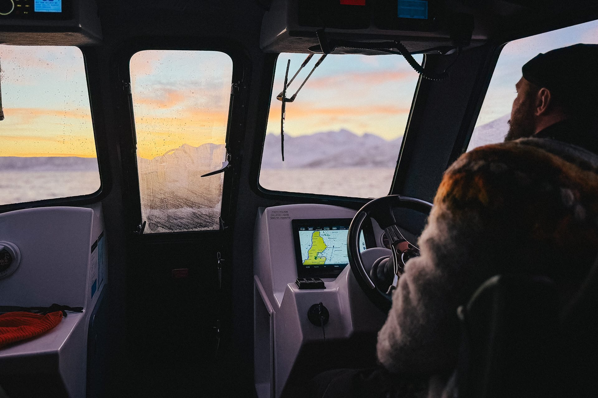 Vista interna della cabina di comando di un'imbarcazione per whale watching a Skjervøy al termine di una spedizione. Strumentazione nautica illuminata nel buio, attrezzatura tecnica in primo piano e vista sfocata delle luci del porto artico in lontananza.