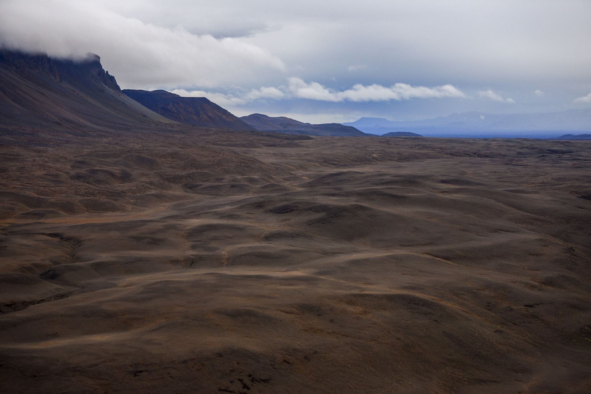 Vasta panoramica desolata del deserto di tefra nera negli altopiani centrali d'Islanda, senza vegetazione né acqua, sotto un cielo grigio e pesante tipico del clima artico.