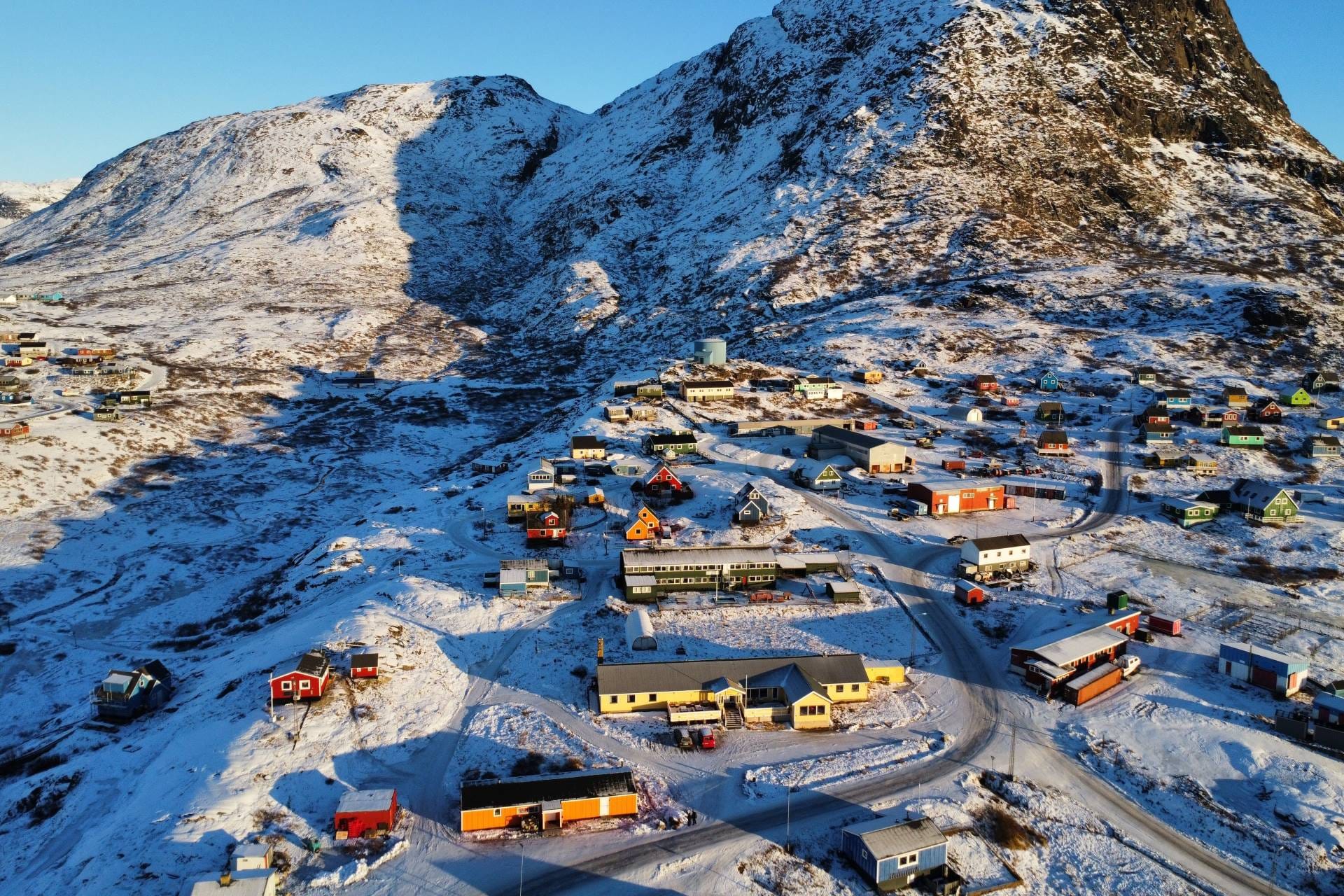 Panoramica aerea invernale dell'insediamento di Narsaq e del fiordo ghiacciato in Groenlandia, epicentro logistico per le risorse naturali artiche.