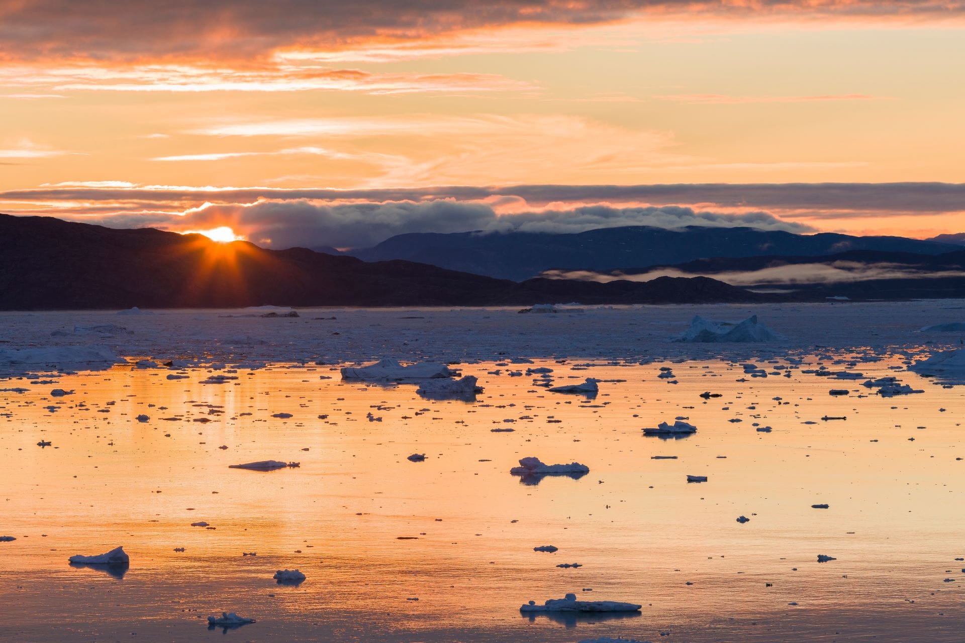 Tramonto sul fiordo ghiacciato presso il ghiacciaio Eqip in Groenlandia, con ombre scure che si allungano sugli iceberg e sull'acqua.